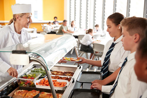 Cafeteria worker serving food to a line of school children